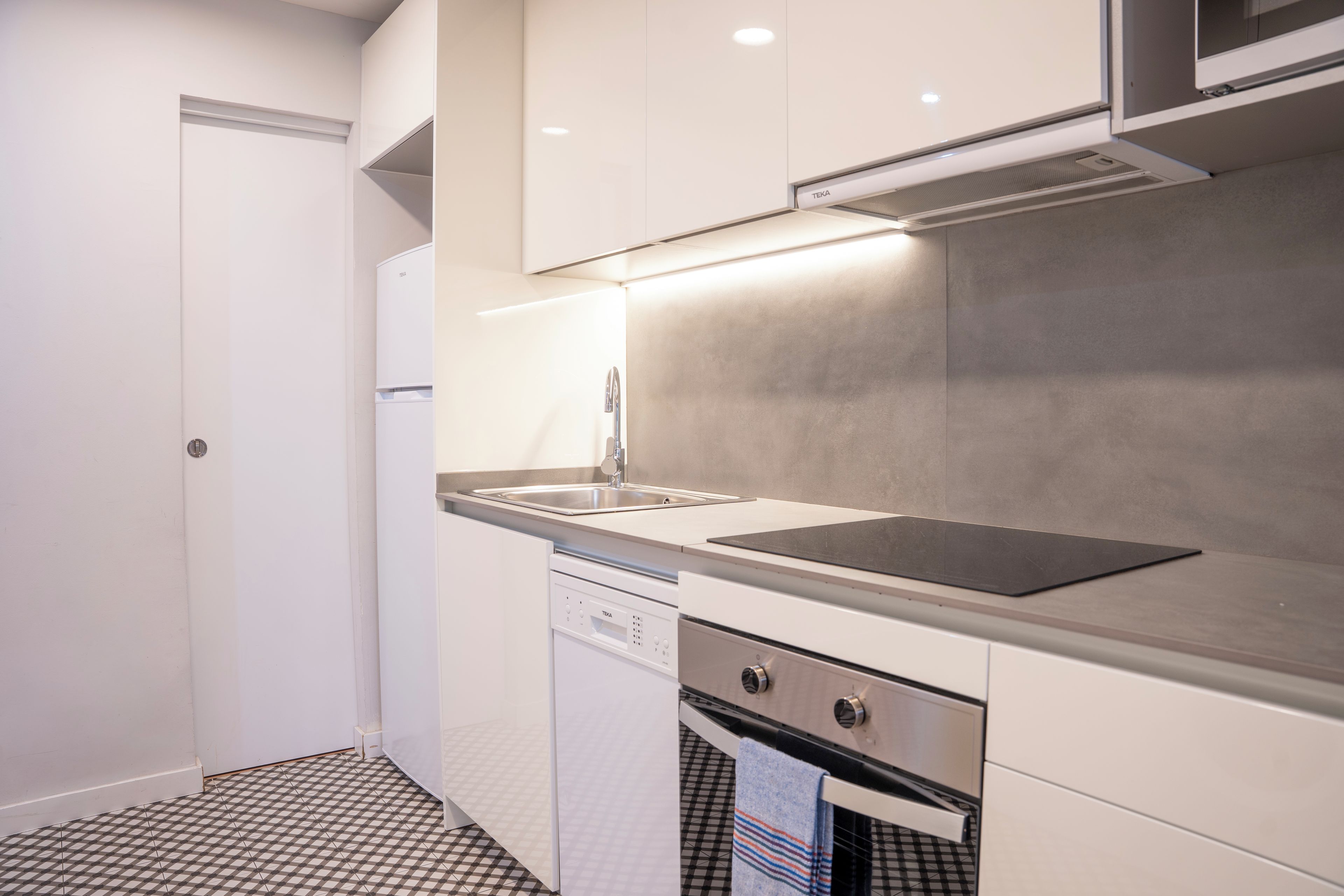 A compact kitchen with white cabinetry, a stainless steel sink, a dishwasher, and a stove.