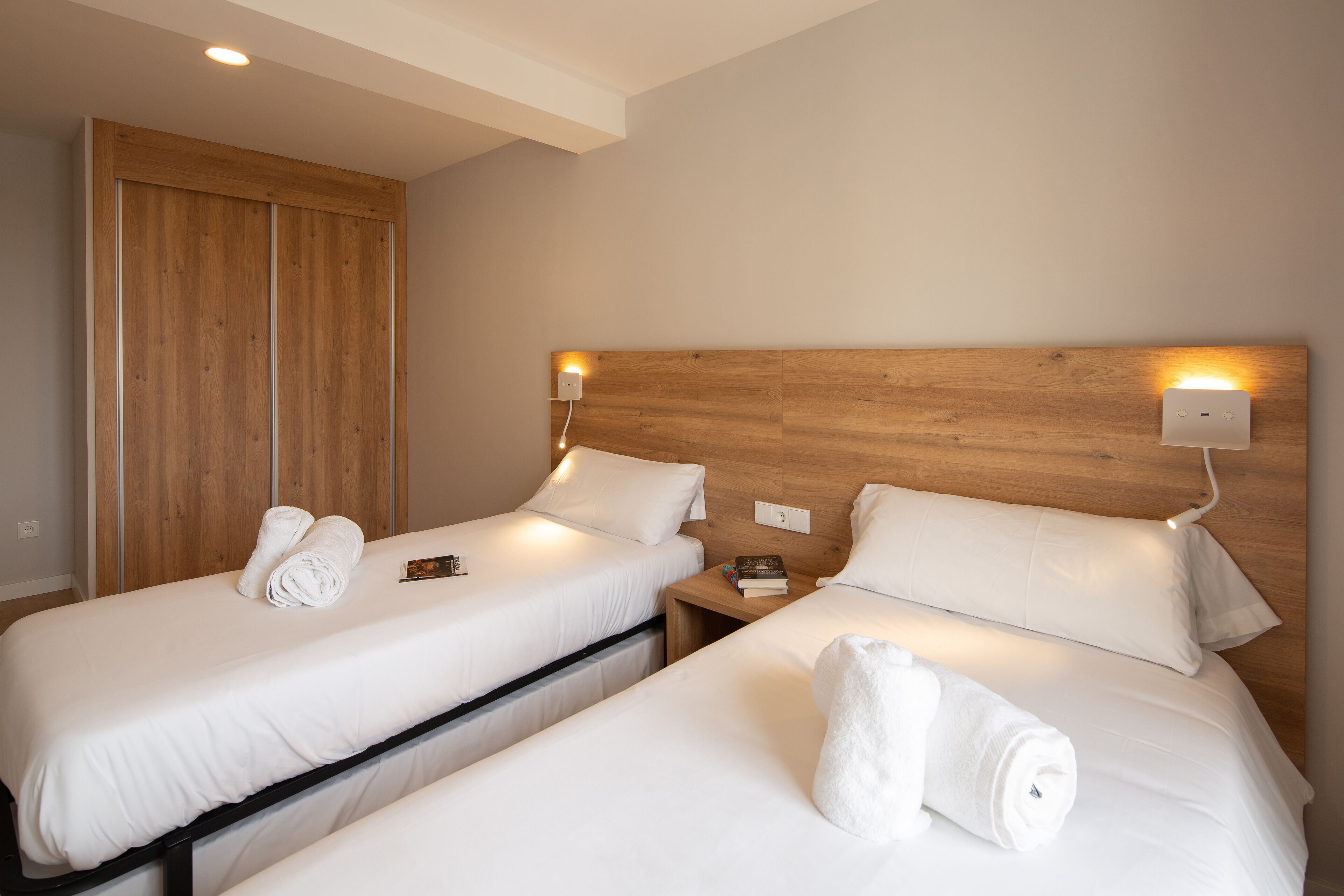 A hotel room with two single beds, wooden headboards, bedside tables, and a wooden wardrobe.