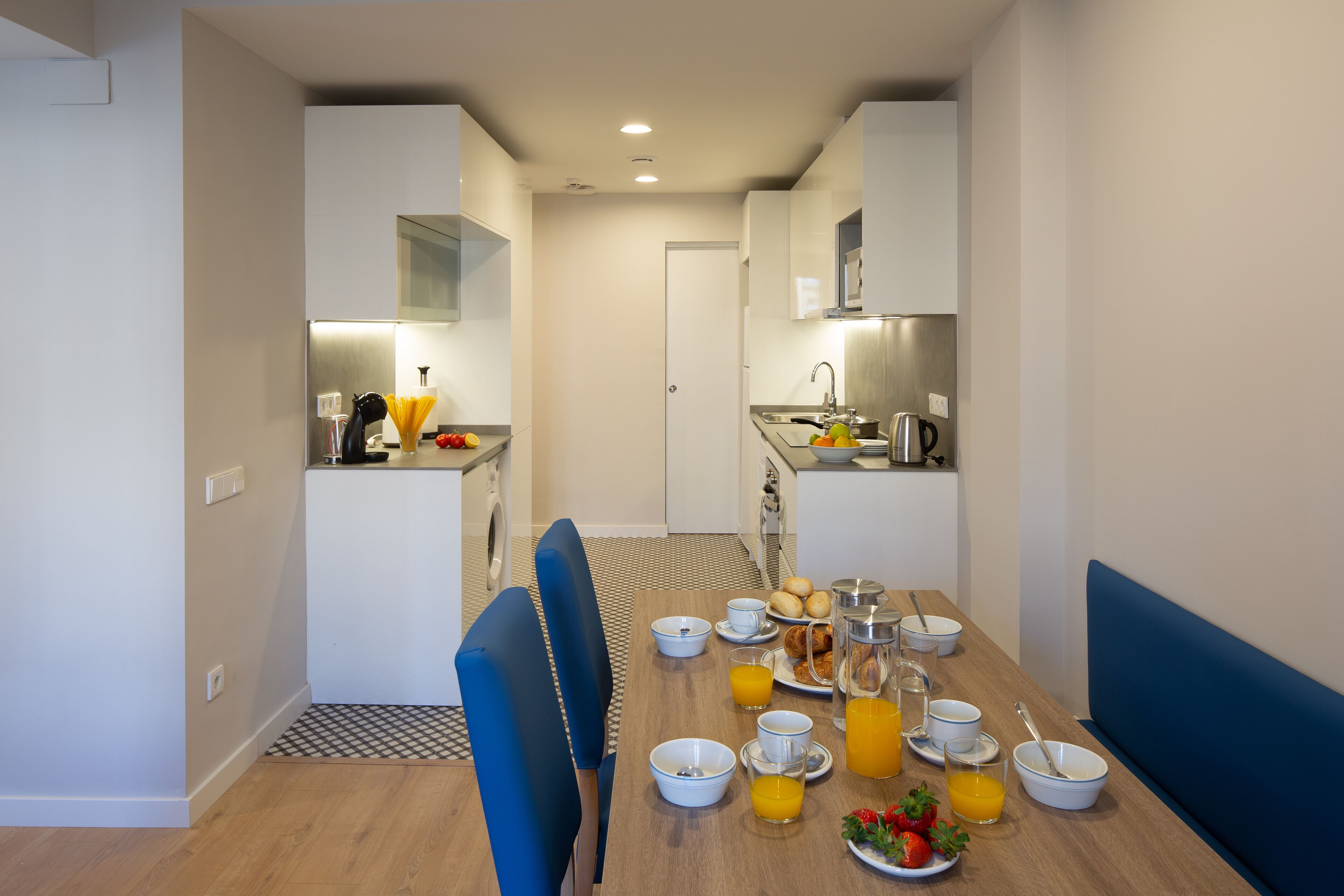 A modern kitchen with white cabinets, a dining table set with breakfast items, and a blue bench.