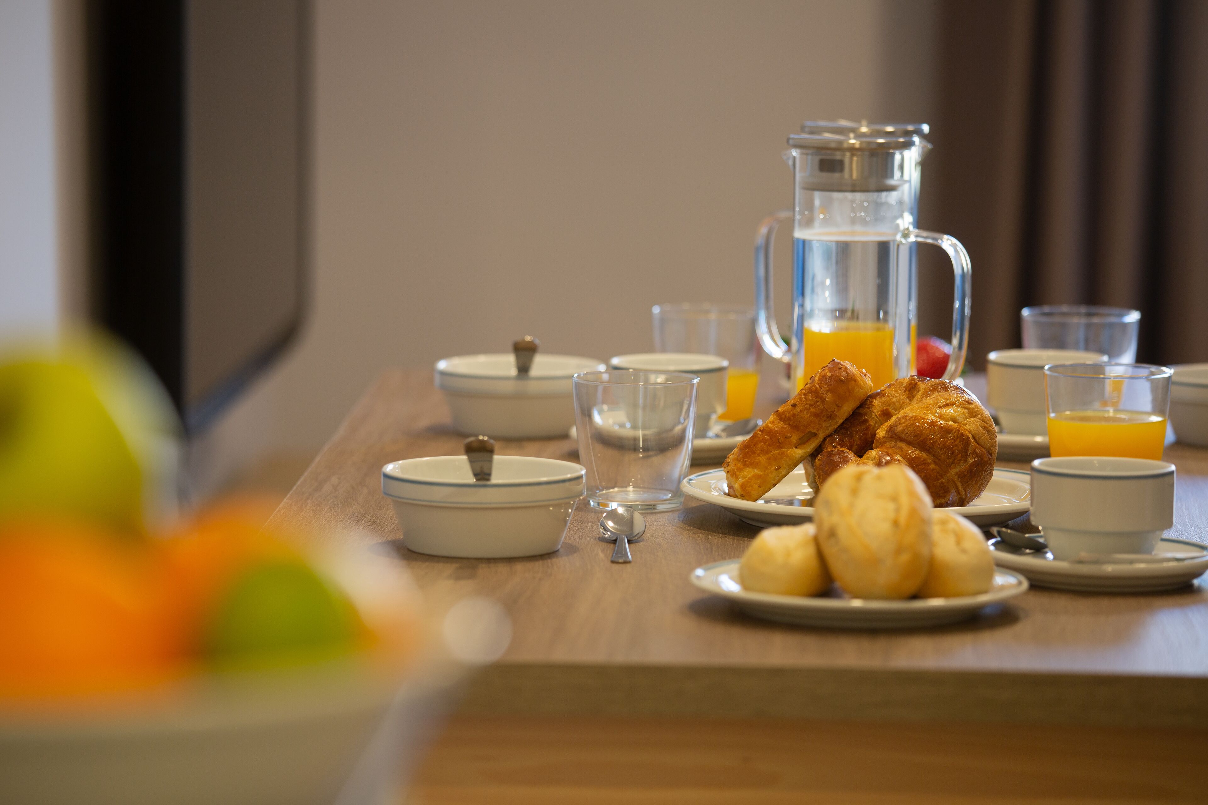 A breakfast table with croissants, orange juice, and a pitcher of water.