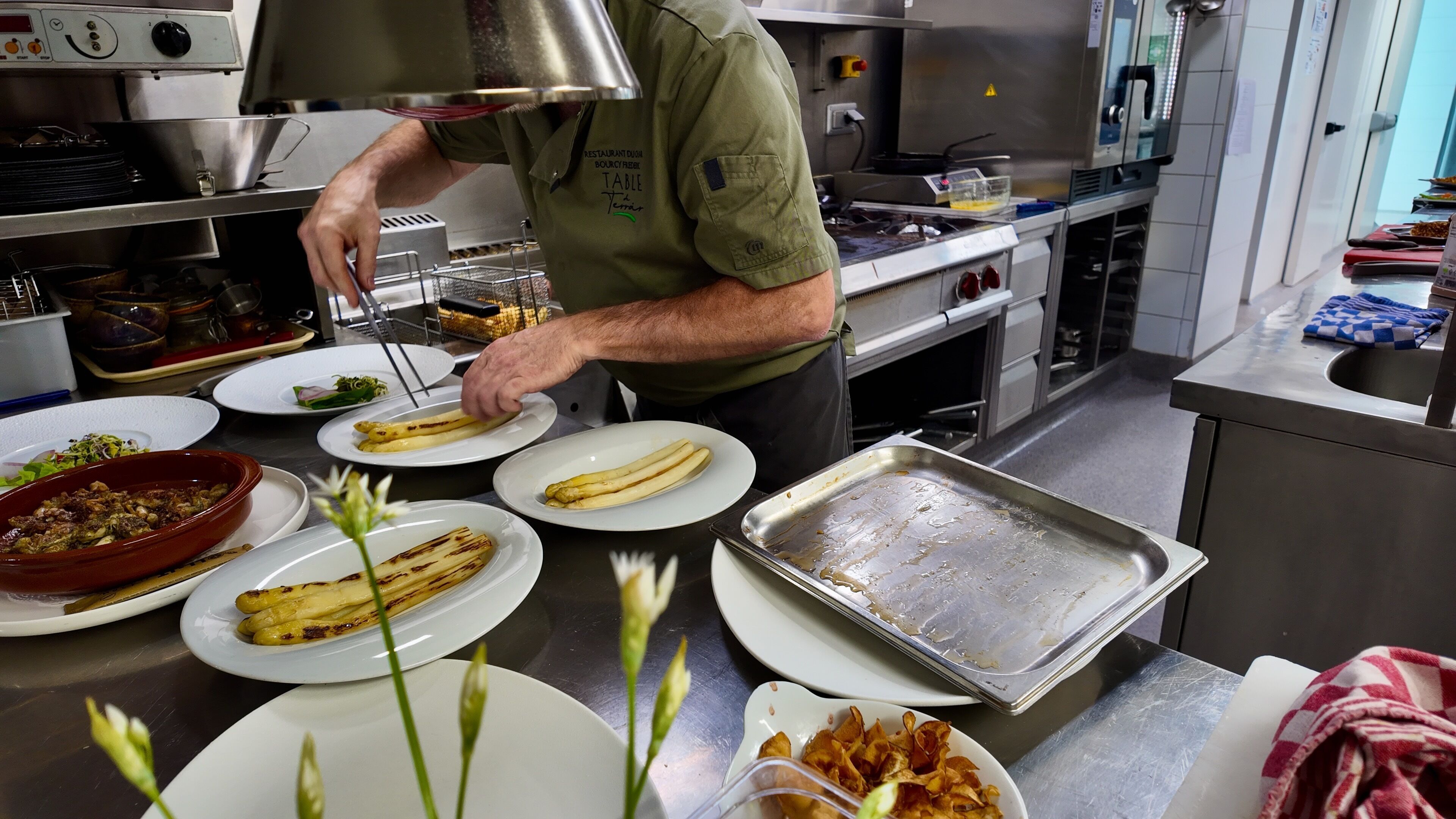 A kitchen with stainless steel appliances, a chef preparing food, and various dishes on plates.