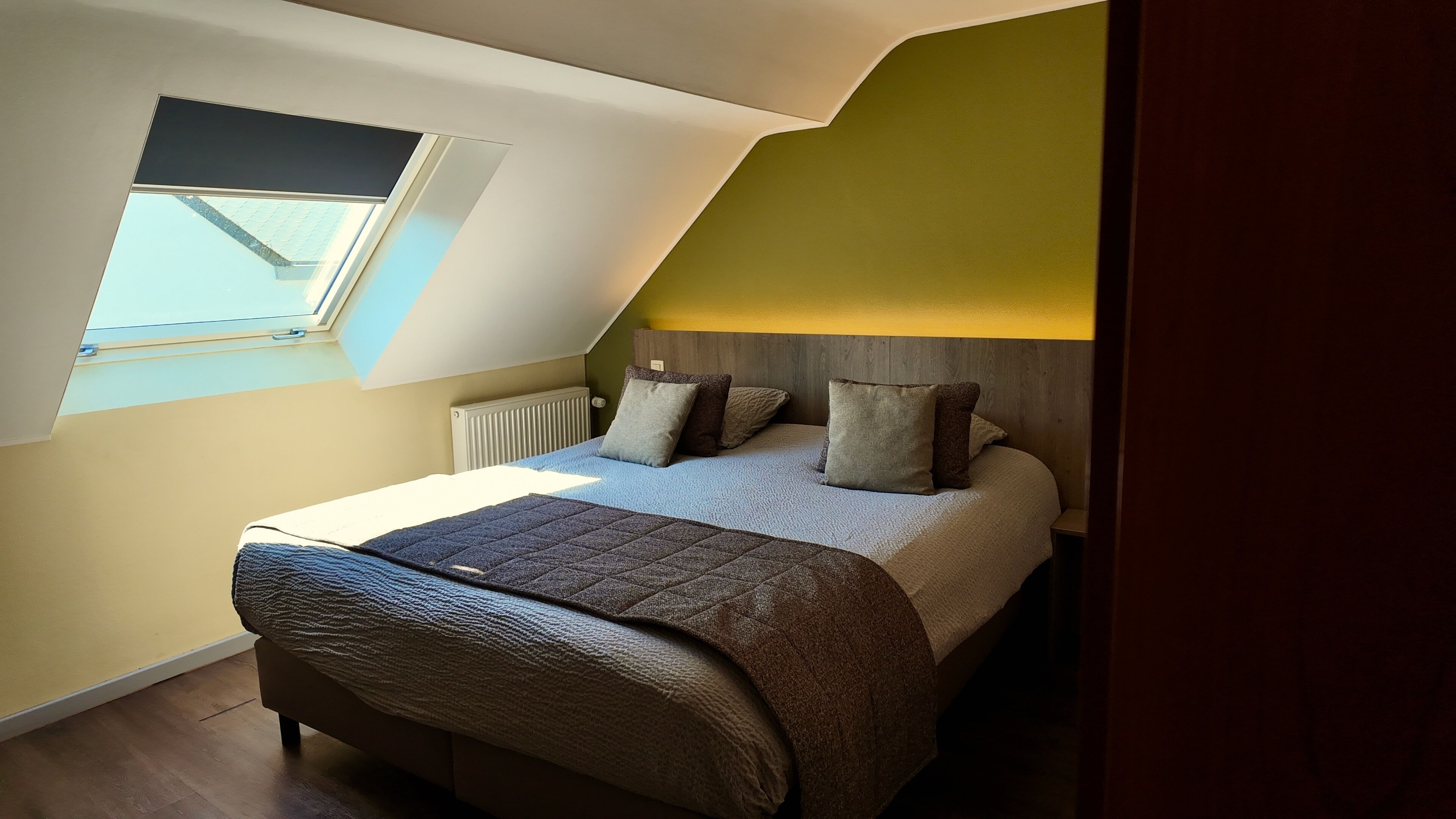 A bedroom with a sloped ceiling, a skylight, a bed with pillows, and a radiator.