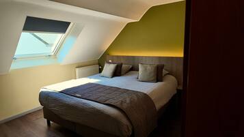A bedroom with a sloped ceiling, a skylight, a bed with pillows, and a radiator.