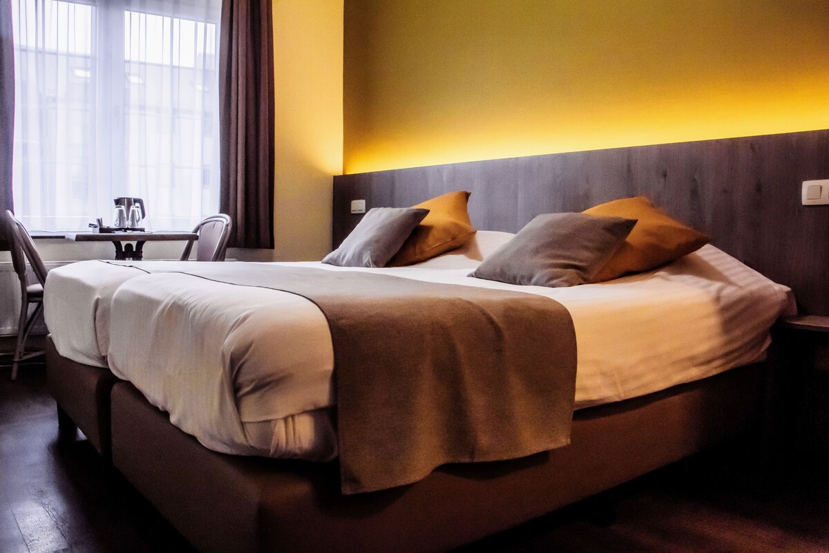 Quarto de hotel com cama, mesa de cabeceira e pequena escrivaninha com cadeira.