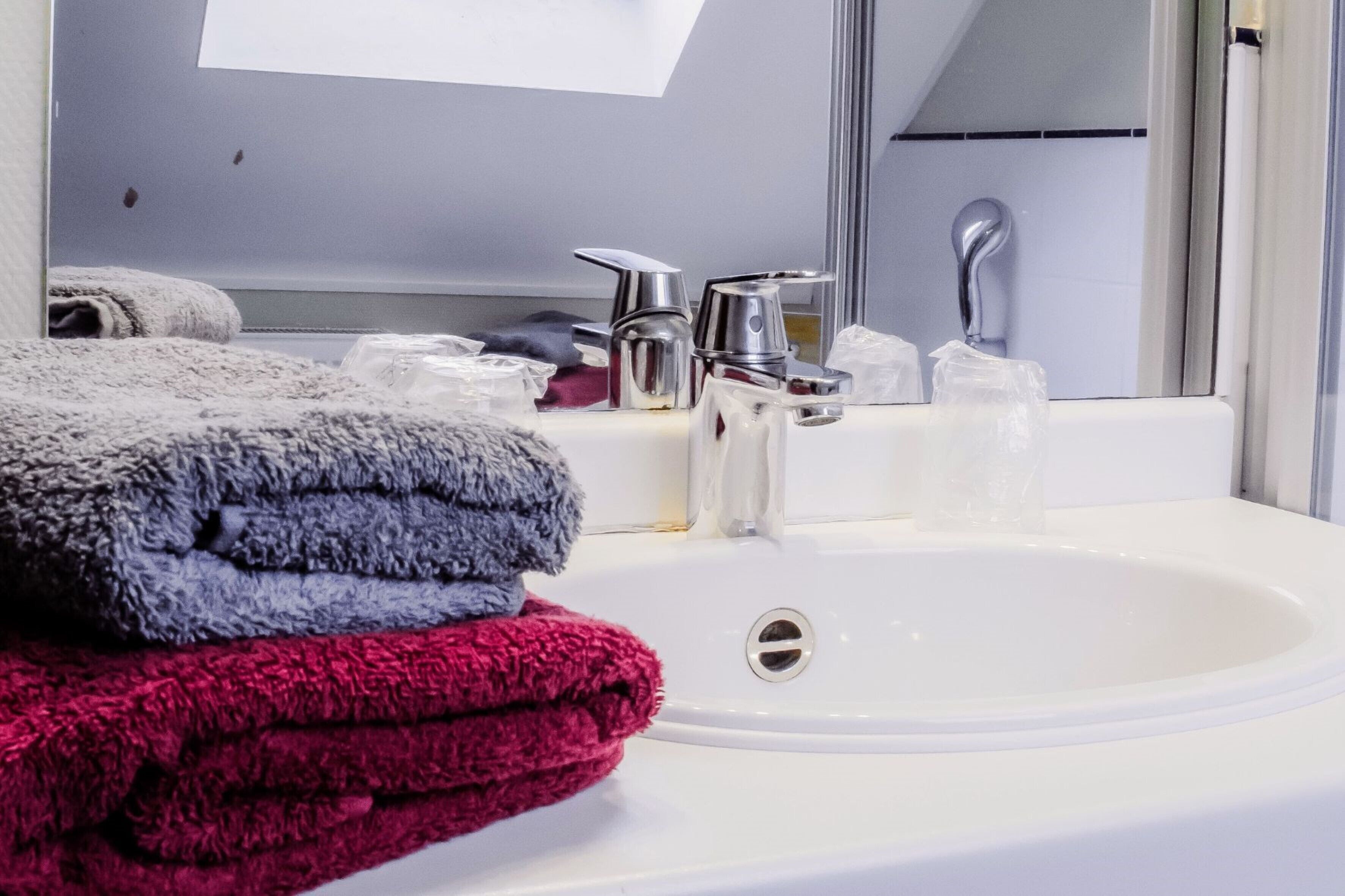 Un baño con un lavamanos blanco, un espejo y un perchero con toallas dobladas.