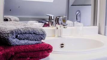 Un baño con un lavamanos blanco, un espejo y un perchero con toallas dobladas.