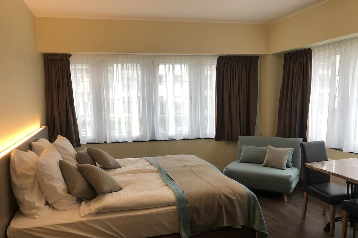 A hotel room with a bed, a sofa, a dining table, and curtains.