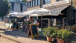 Un restaurante con terraza, un letrero que dice 'Hotel des Postes' y un menú en la pizarra.