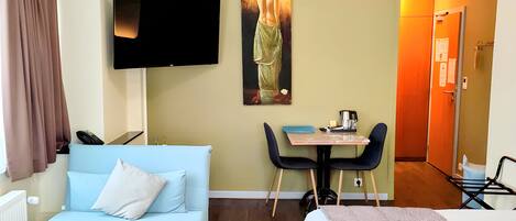 A hotel room with a light blue sofa, a bed, a dining table with chairs, a flat-screen TV, and a painting on the wall.