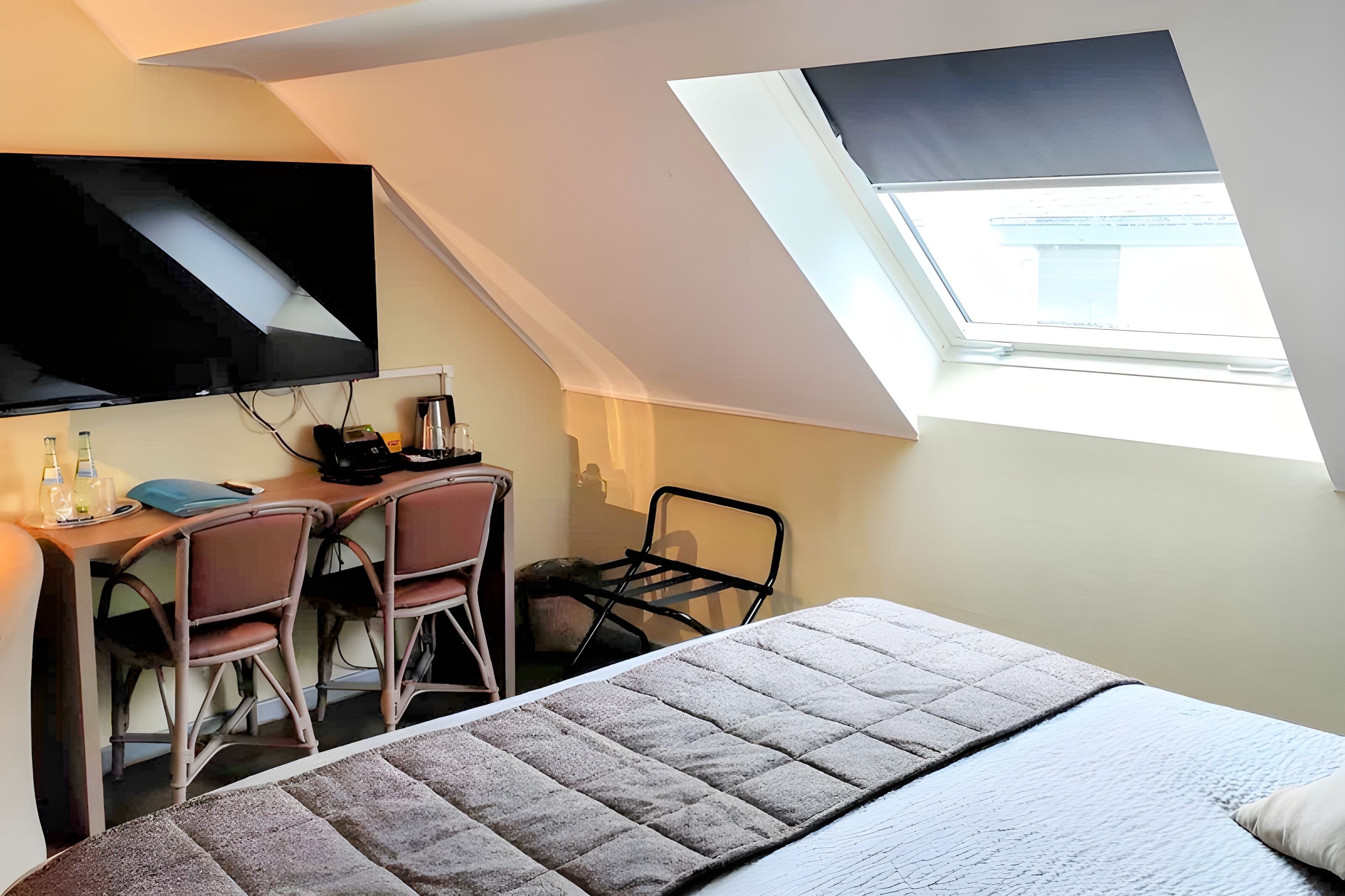 Une chambre à coucher avec un lit, un bureau avec deux chaises, une télévision et une lucarne.