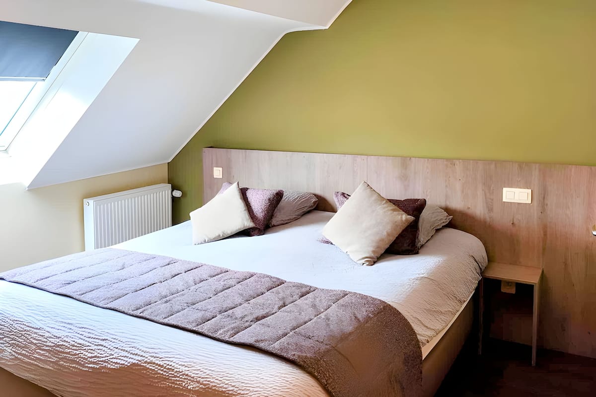 A bedroom with a sloped ceiling, a bed with a headboard, two bedside tables, and a window.