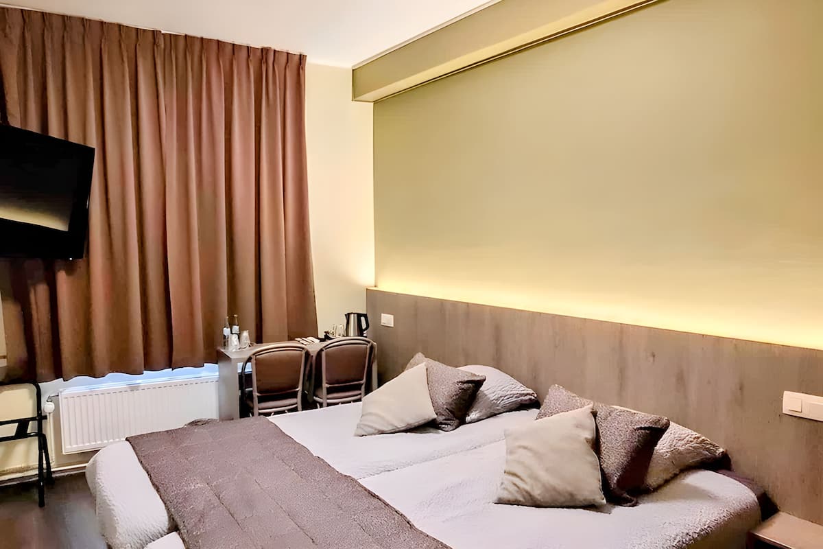 A hotel room with a bed, a desk with chairs, a television, and a window with curtains.