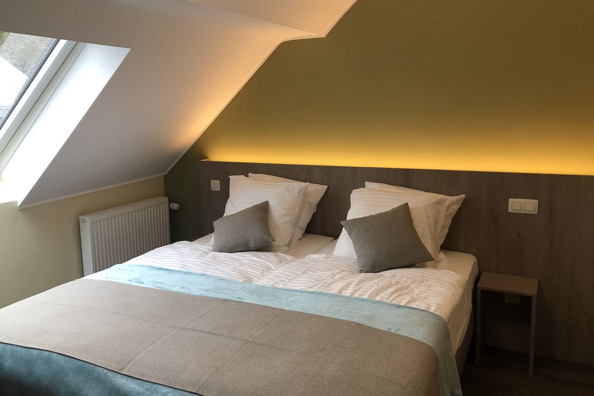 A bedroom with a sloped ceiling, a bed with white linens, and a small bedside table.