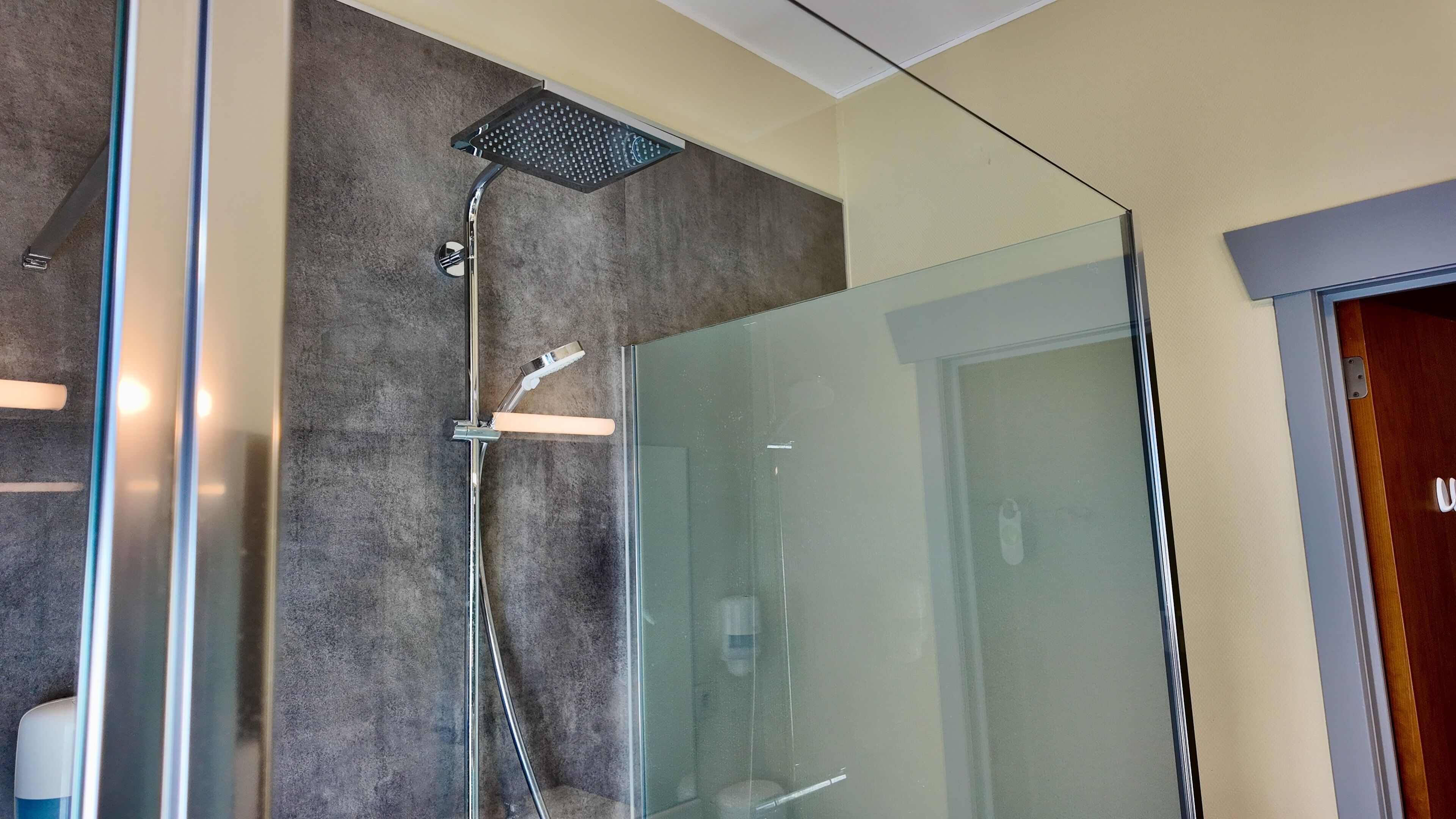 A modern bathroom with a glass shower enclosure, a visible toilet, and a door with a handle.