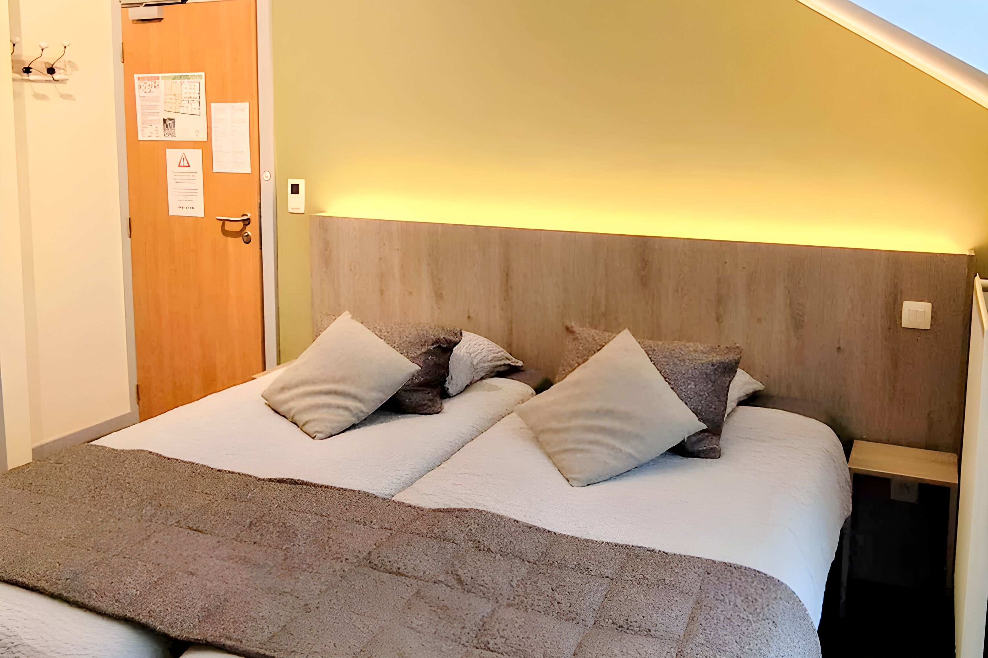 Un lit double avec deux oreillers, une tête de lit en bois, une table de chevet et une lampe fixée au mur.