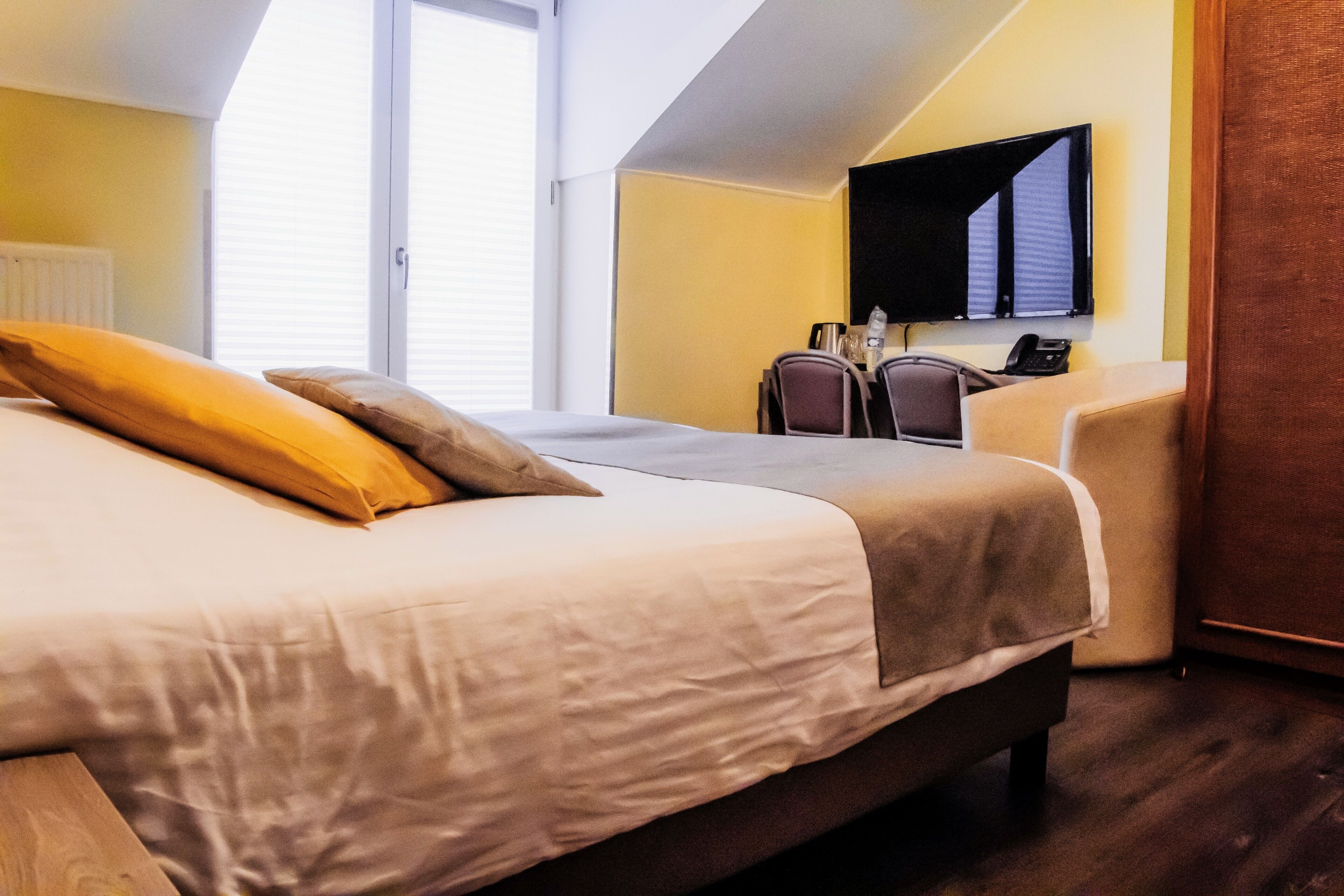 Quarto de hotel com uma cama grande, uma escrivaninha com cadeira, televisão e janela com persianas.
