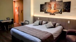 Habitación de hotel con una cama grande, un escritorio y una silla. Hay una obra de arte en la pared sobre la cama.
