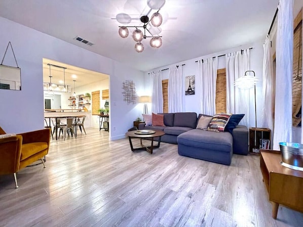 A modern living room with a grey sofa, a wooden coffee table, and a dining area with a wooden table and chairs.