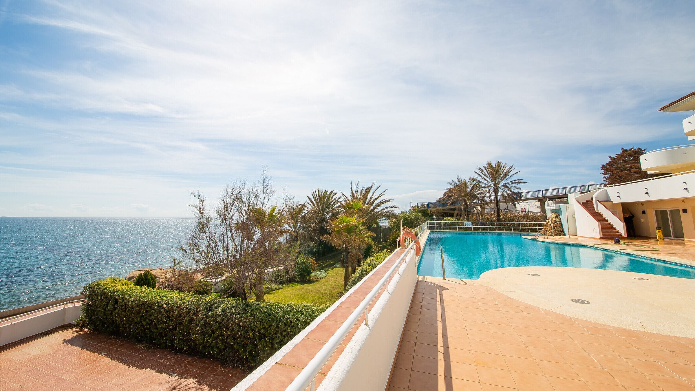 Vista a la piscina con una imagen despejada del mar, un jardín cuidado y un edificio moderno con balcón.