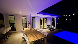 A modern dining area with a wooden table and white chairs, a small indoor pool with blue lighting, and a separate lounge area with a pool table and chairs. - Lxry Apartment Jan Sofat With Private Pool (Willemstad)
