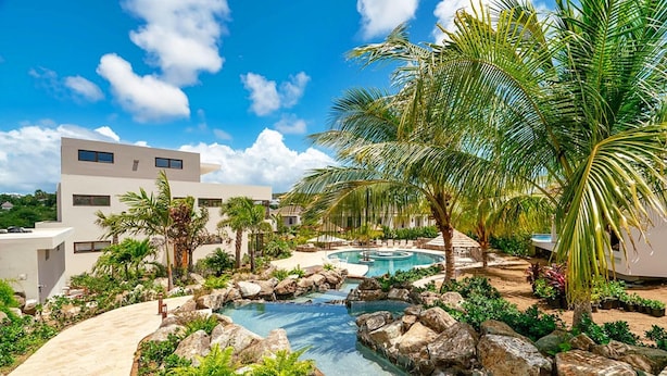 A modern resort with a swimming pool, palm trees, and a rocky water feature. - Lxry Apartment Jan Sofat With Private Pool (Willemstad)
