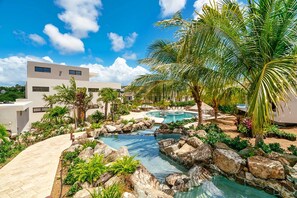 A modern resort with a swimming pool, palm trees, and a rocky water feature.