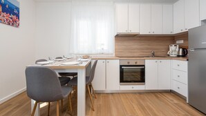 Et moderne køkken med hvide skabe, en træbordplade, indbygget ovn og et rustfrit stål køleskab.