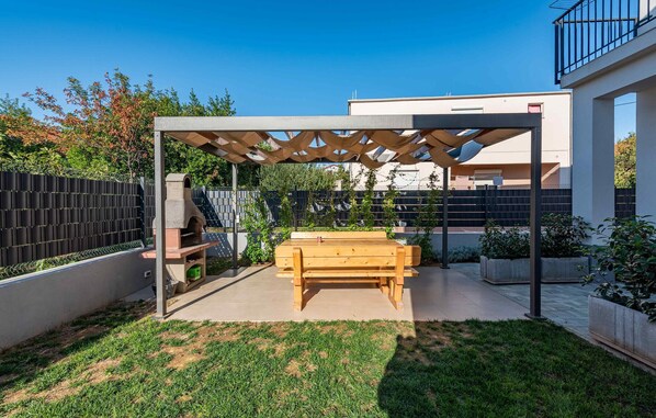 Un patio couvert avec une table et des chaises en bois, un barbecue et une structure en forme de pergola.