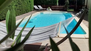 Una piscina con una hamaca, sillas de descanso y una terraza de madera.