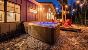 Un bain à remous à l’extérieur d’un bâtiment en bois, avec une terrasse et des chaises.