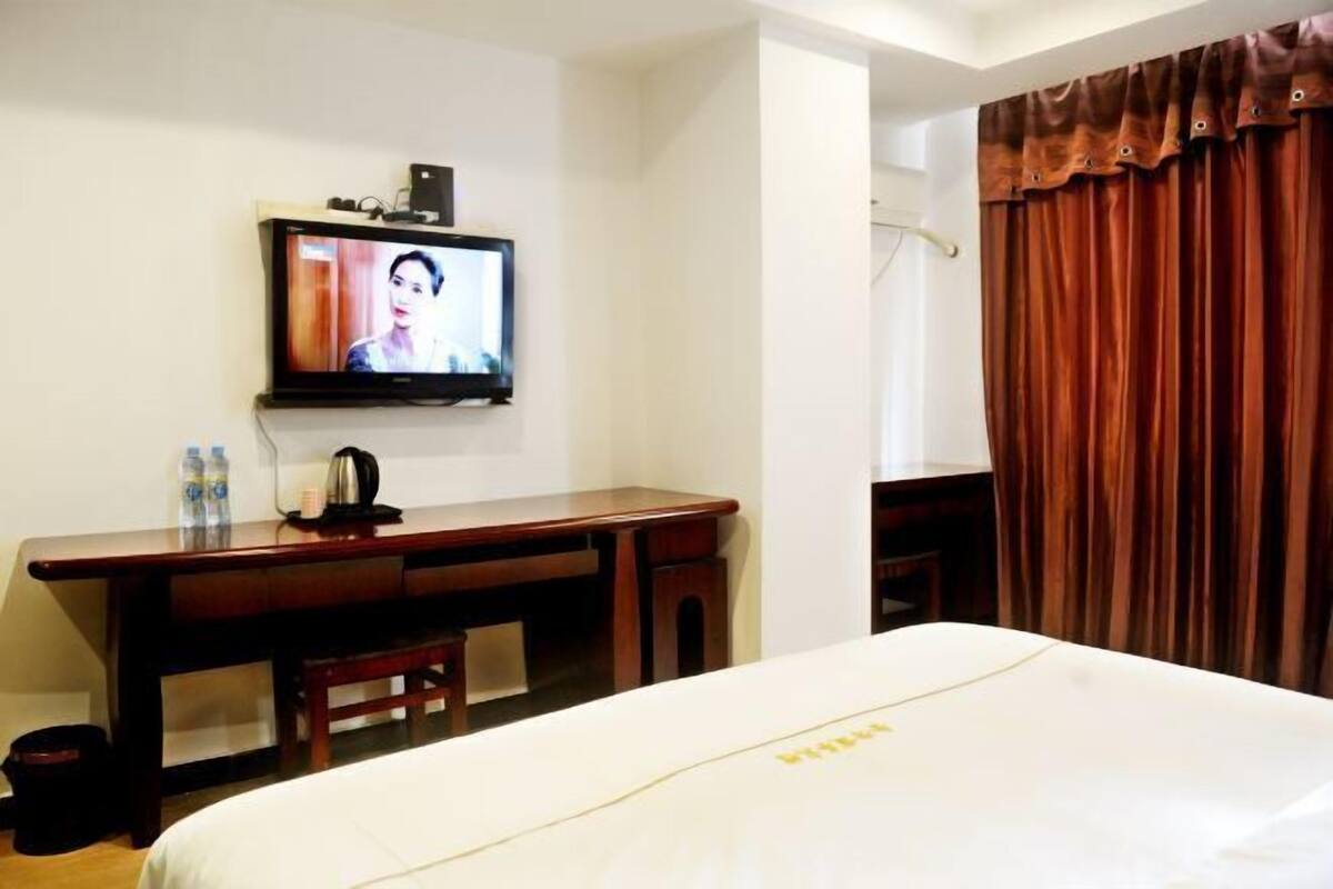 A hotel room with a bed, a desk with a television, a coffee maker, and a window with curtains.