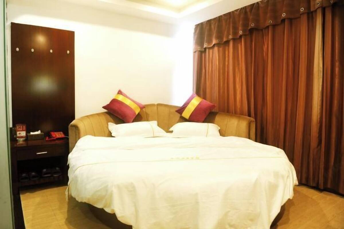 A hotel room with a large bed, a wooden wardrobe, and a curtain.