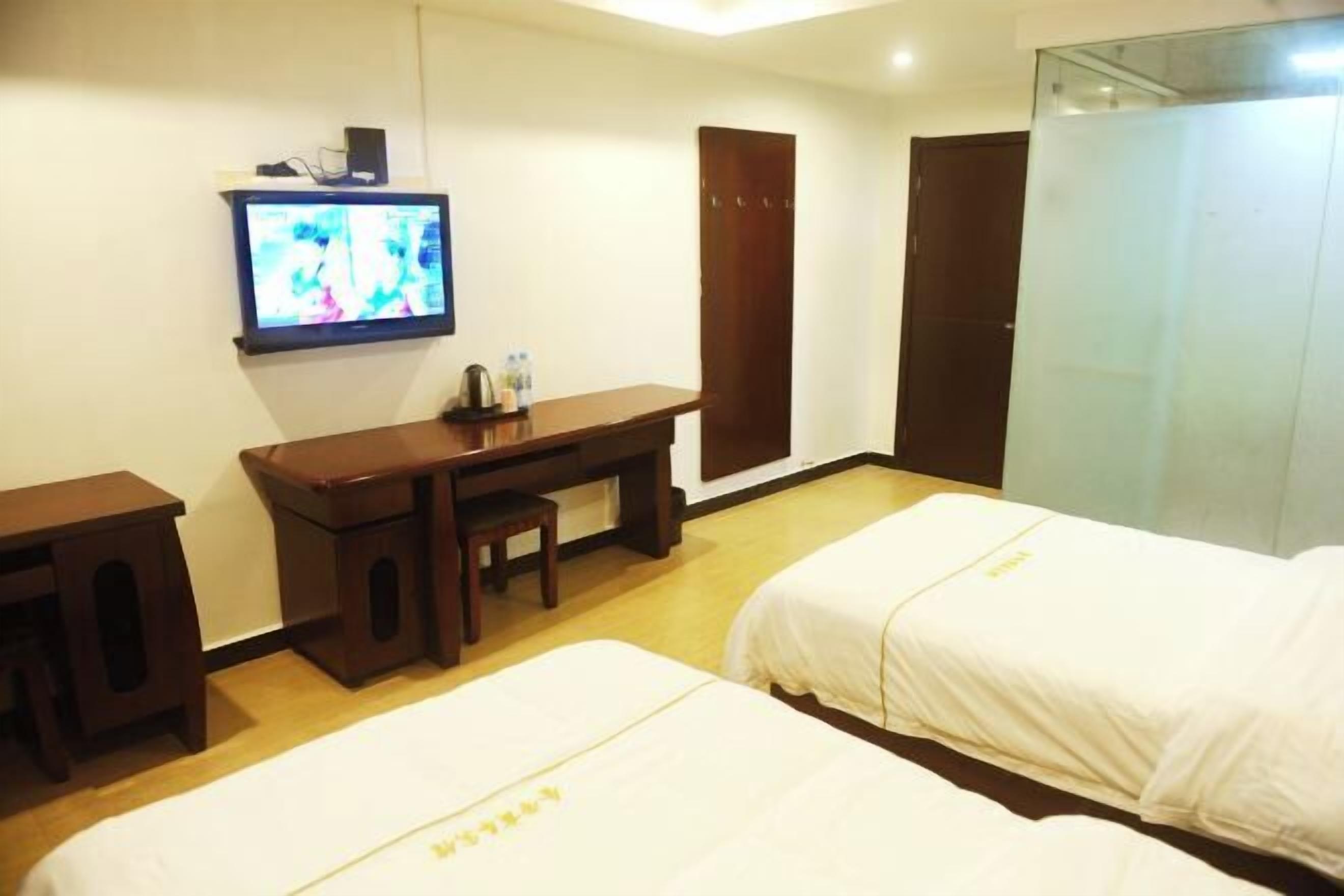 Una habitación de hotel con dos camas, un escritorio con una silla, un televisor y un armario.