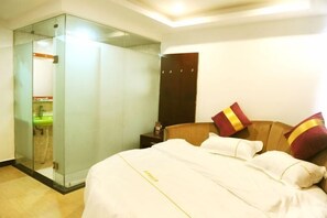 Une chambre d’hôtel avec un lit, une tête de lit en bois et une douche séparée par des parois en verre.