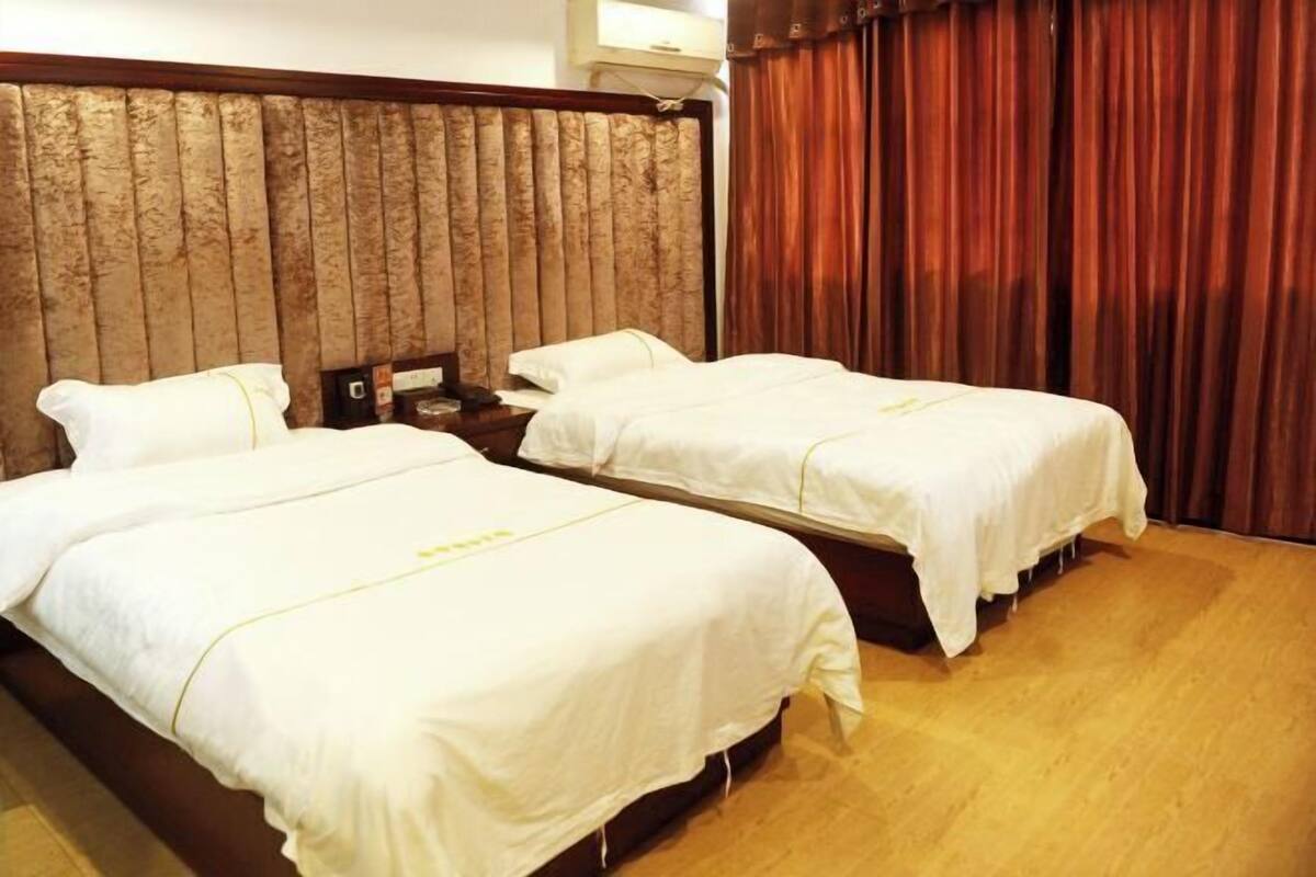 A hotel room with two beds, wooden headboard, and a curtain.