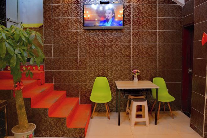A small dining area with a TV mounted on the wall, a staircase with orange steps, and two green chairs.