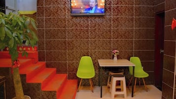 A small dining area with a TV mounted on the wall, a staircase with orange steps, and two green chairs.