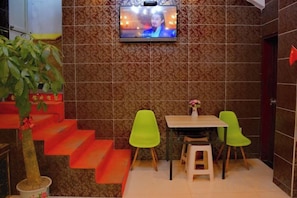 A small dining area with a TV mounted on the wall, a staircase with orange steps, and two green chairs. - Nanchang Jindi Hotel (Bayiguan Subway Station Branch) (Nanchang)