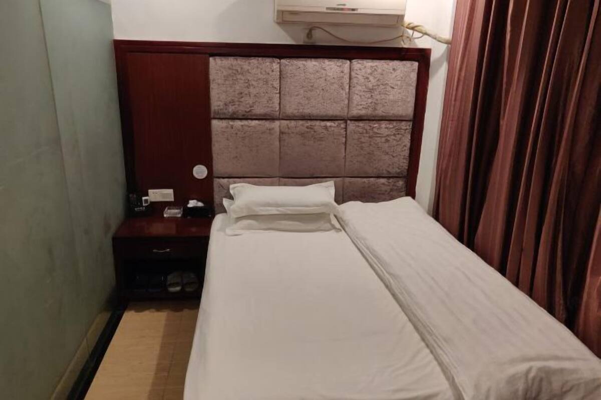 A small, neatly made bed with a wooden headboard and a nightstand beside it.
