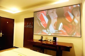 Une chambre d’hôtel équipée d’un lit, d’un bureau et d’un grand écran diffusant un film.