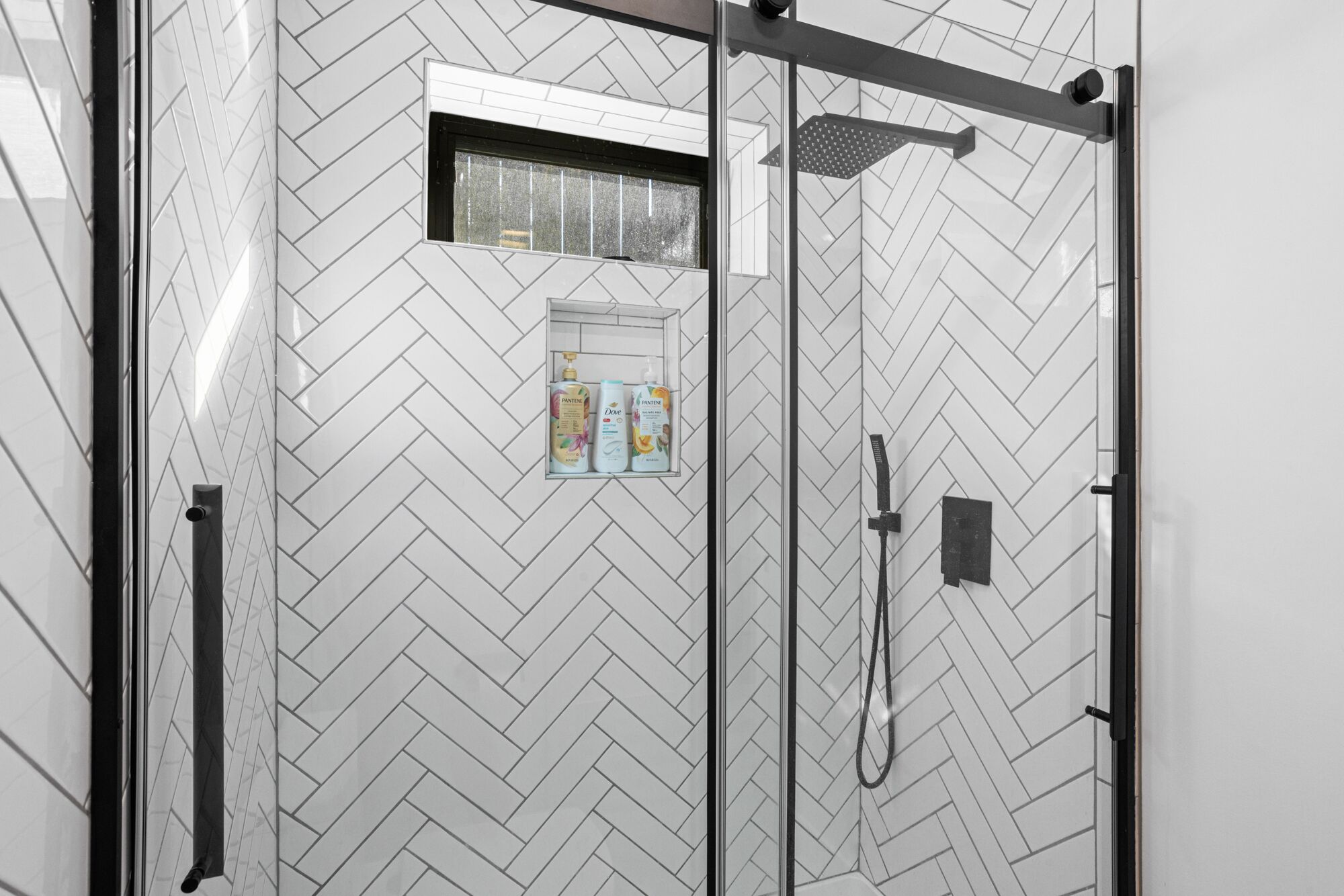 Eine moderne Dusche mit Zickzack-Fliesenmuster, einem Fenster und einem Wandspender für Seife.