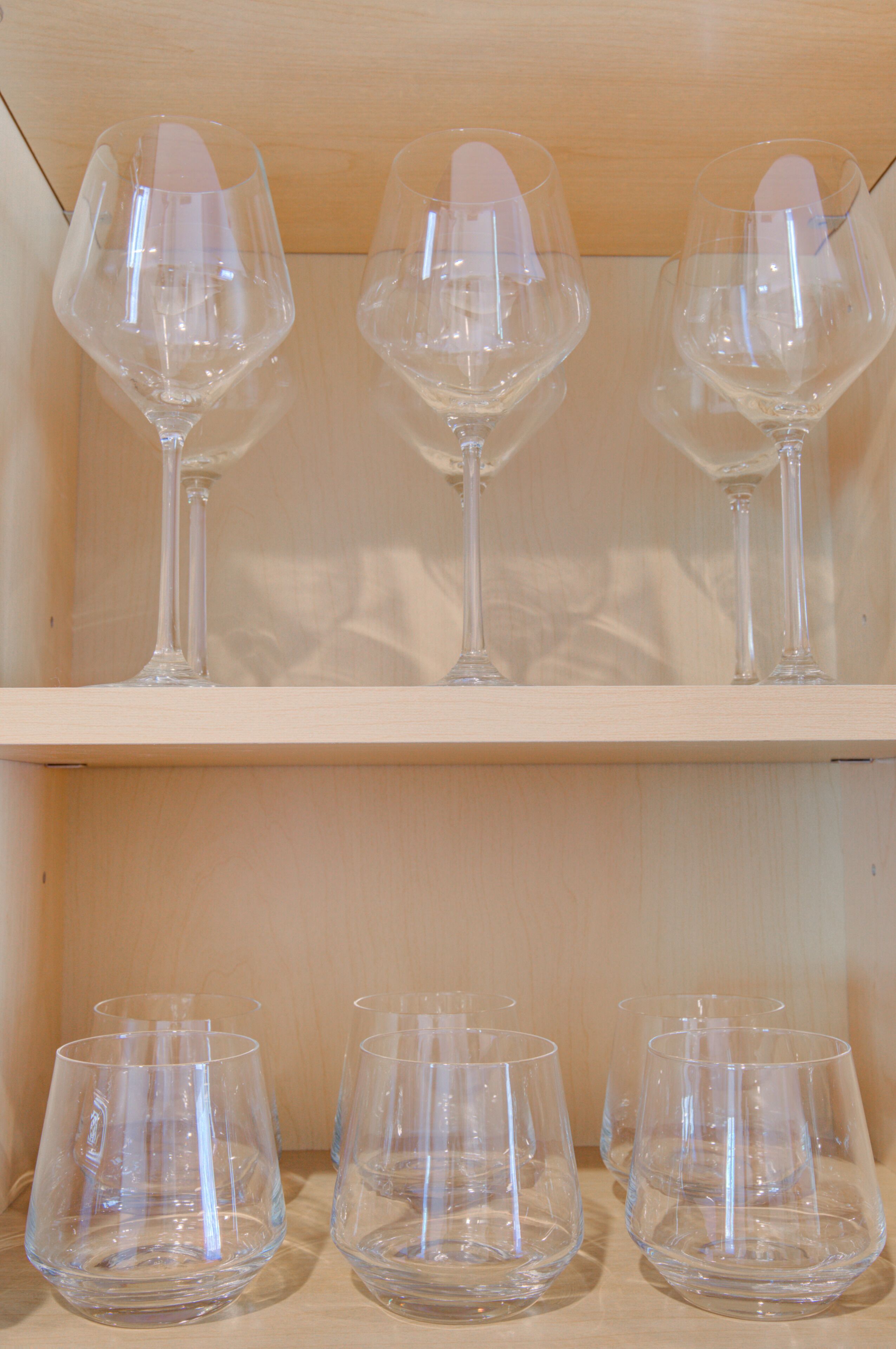 A wooden shelf with three wine glasses on the top and four on the bottom.