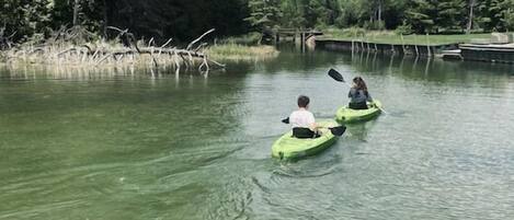 Dos personas remando en kayak por un río tranquilo bordeado de árboles frondosos.