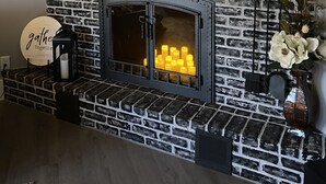 A fireplace with a brick wall, a clock, and a shelf with decorative items.