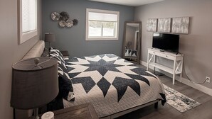 A bedroom with a bed, bedside table, lamp, TV stand, and a window.