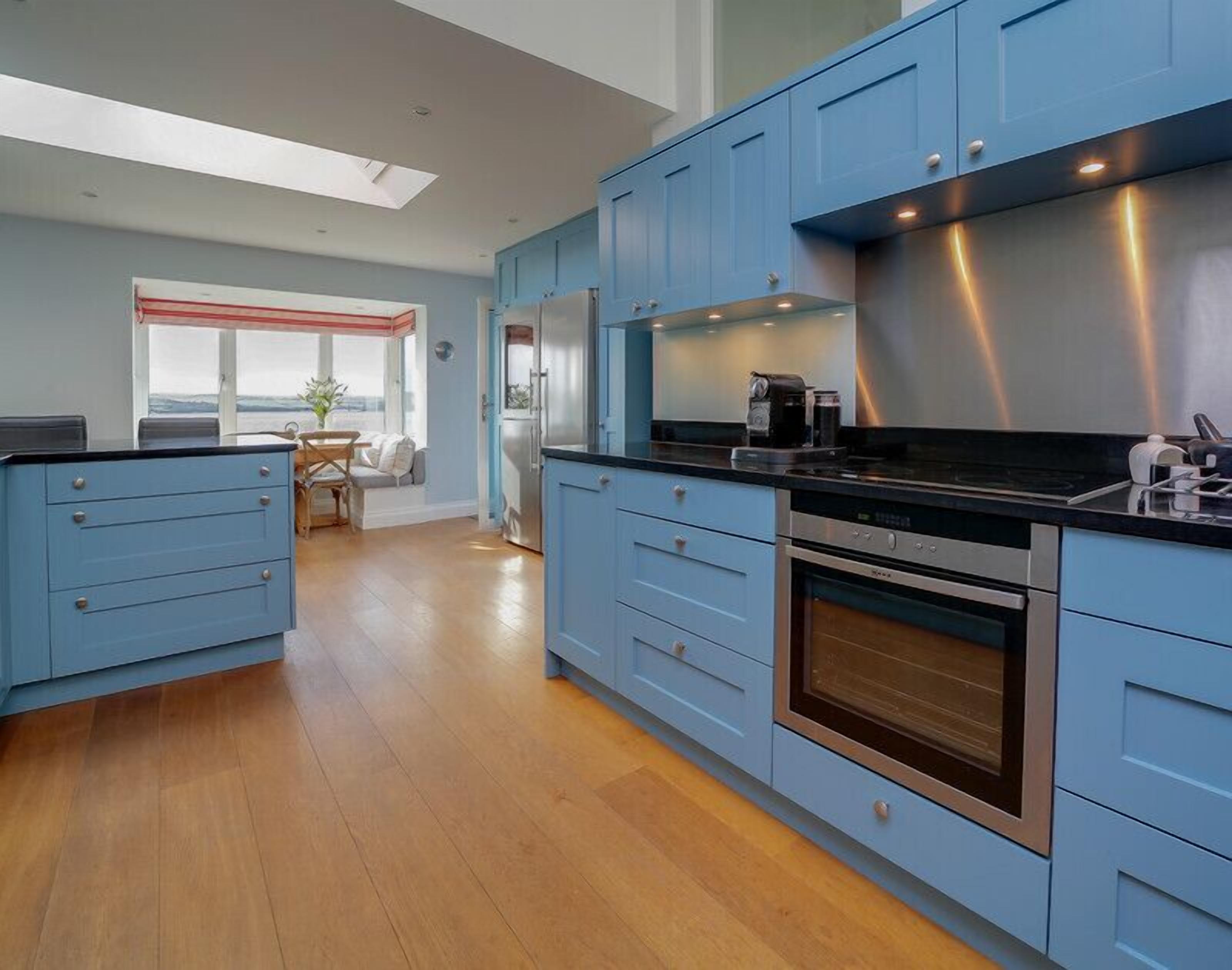 A modern kitchen with blue cabinets, a stainless steel range hood, and a built-in oven.