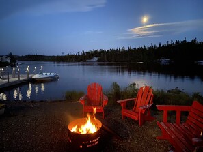 A lakeside scene with a fire pit, red chairs, and a dock with boats. - Couple's Retreat, Beautiful Boathouse on the Water. (Whitbourne)