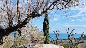 A wooden deck with a stone table and a chair, overlooking a scenic landscape with trees and a view of the sea. - Luxurious Mas with Bassin Balnéo Sea View in Collioure 12 pers (Collioure)