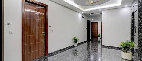 Un pasillo moderno de hotel con suelo de mármol, puertas de madera y ventiladores de techo.