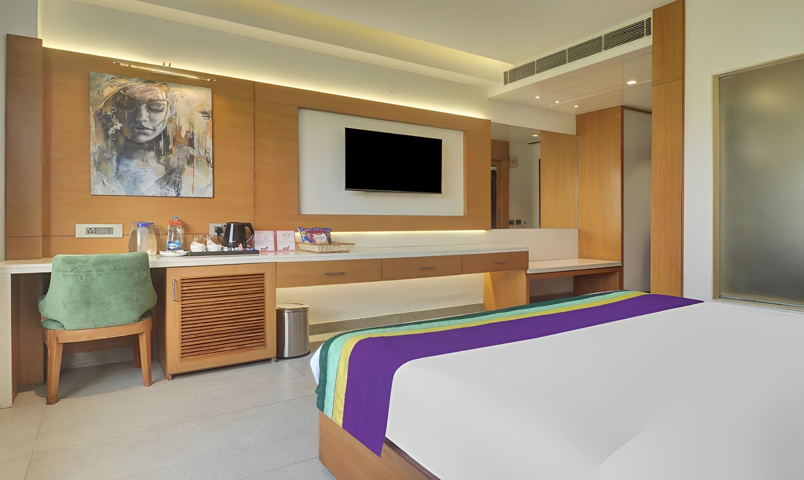 Una habitación de hotel moderna con una cama grande, un escritorio con silla, un televisor de pantalla plana y un cuadro en la pared.